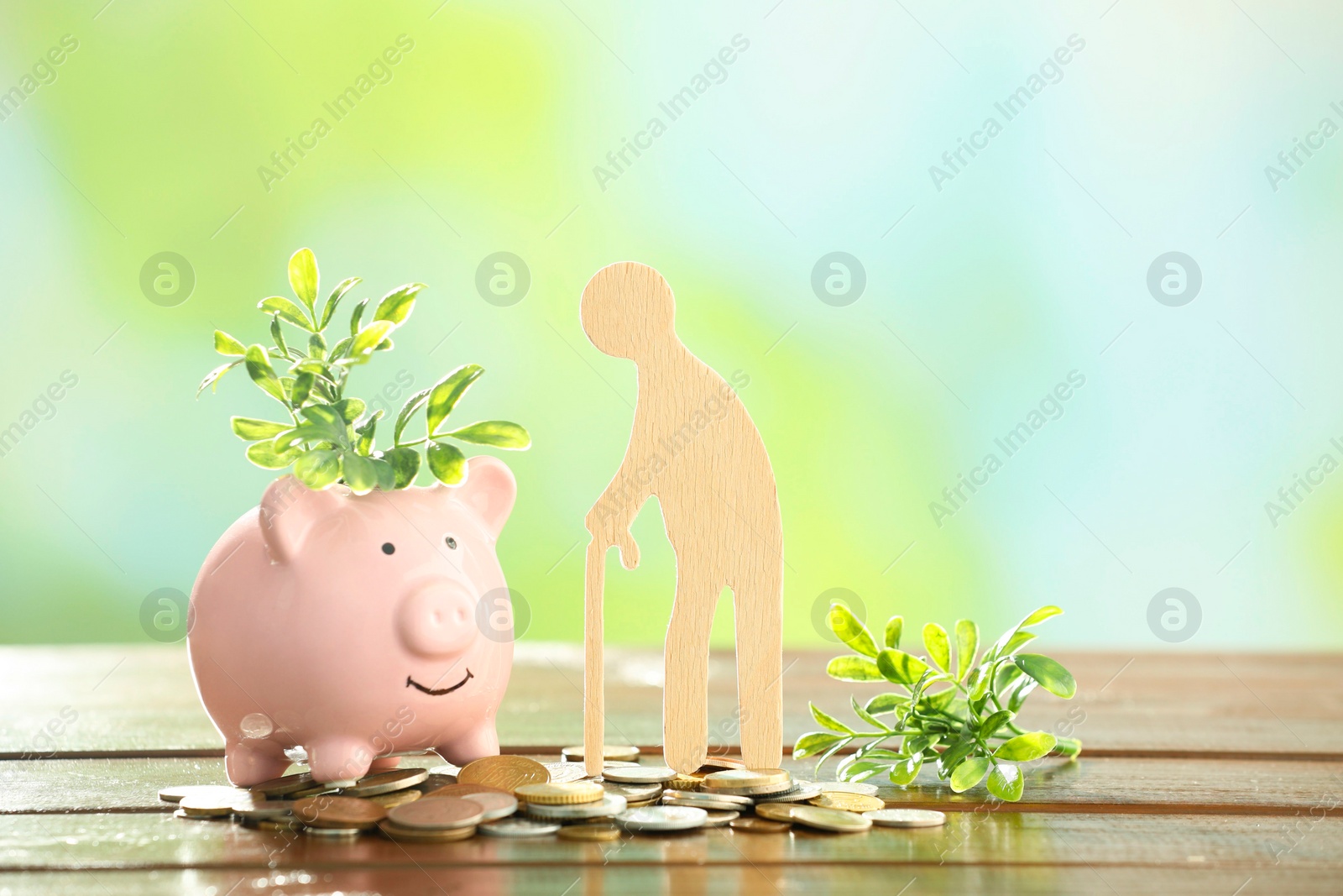 Photo of Pension savings. Figure of senior man, piggy bank, coins and green twigs on wooden table against blurred background