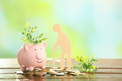 Pension savings. Figure of senior man, piggy bank, coins and green twigs on wooden table against blurred background