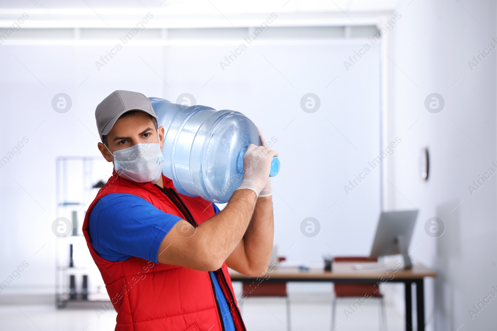 Photo of Courier in mask with bottle of cooler water indoors. Delivery during coronavirus quarantine