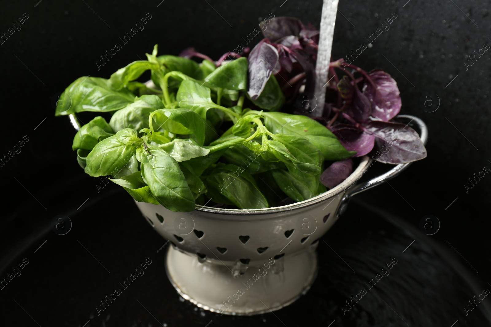 Photo of Washing different fresh basil leaves under tap water in metal colander in sink