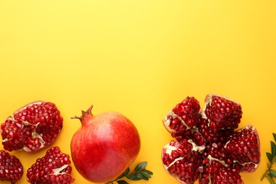 Fresh pomegranates and green leaves on yellow background, flat lay. Space for text