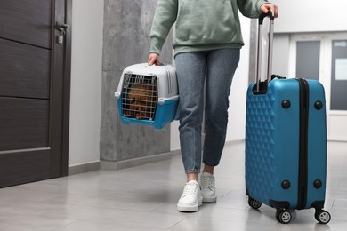 Travel with pet. Woman with suitcase holding carrier with dog indoors, closeup. Space for text