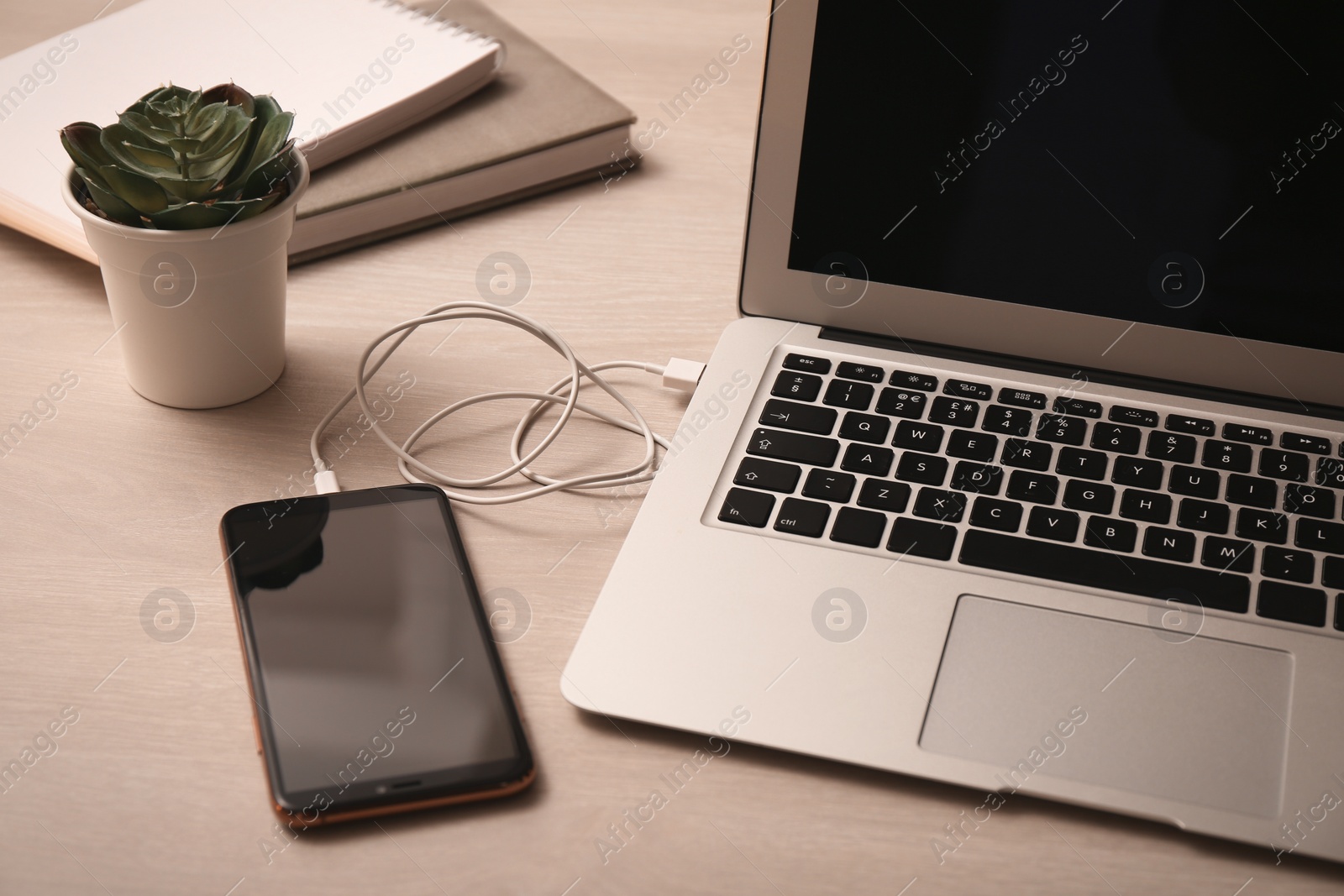 Photo of Smartphone connected with charge cable to laptop on wooden table. Space for text