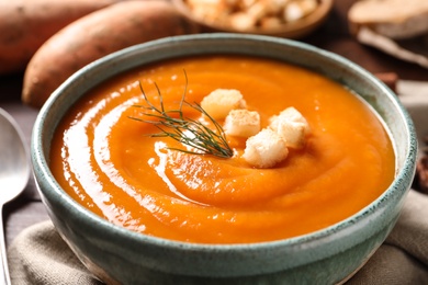 Photo of Bowl of tasty sweet potato soup on table, closeup