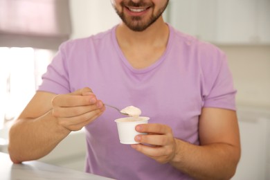 Photo of Happy young man with tasty yogurt at table in kitchen, closeup