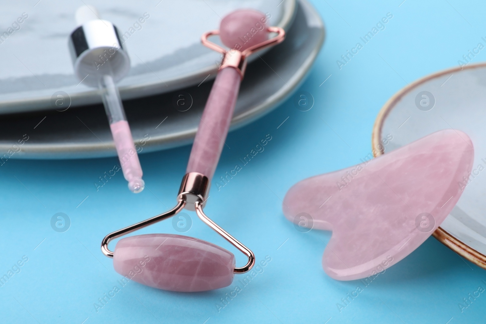 Photo of Rose quartz gua sha tool, facial roller and dropper on light blue background, closeup