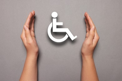 Image of Disability inclusion. Woman protecting wheelchair symbol on grey background, closeup