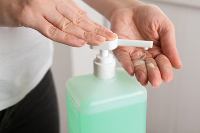 Photo of Woman applying antiseptic gel on hand indoors, closeup