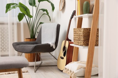 Photo of Spring atmosphere. Wooden shelving unit, acoustic guitar and comfortable chair in stylish room