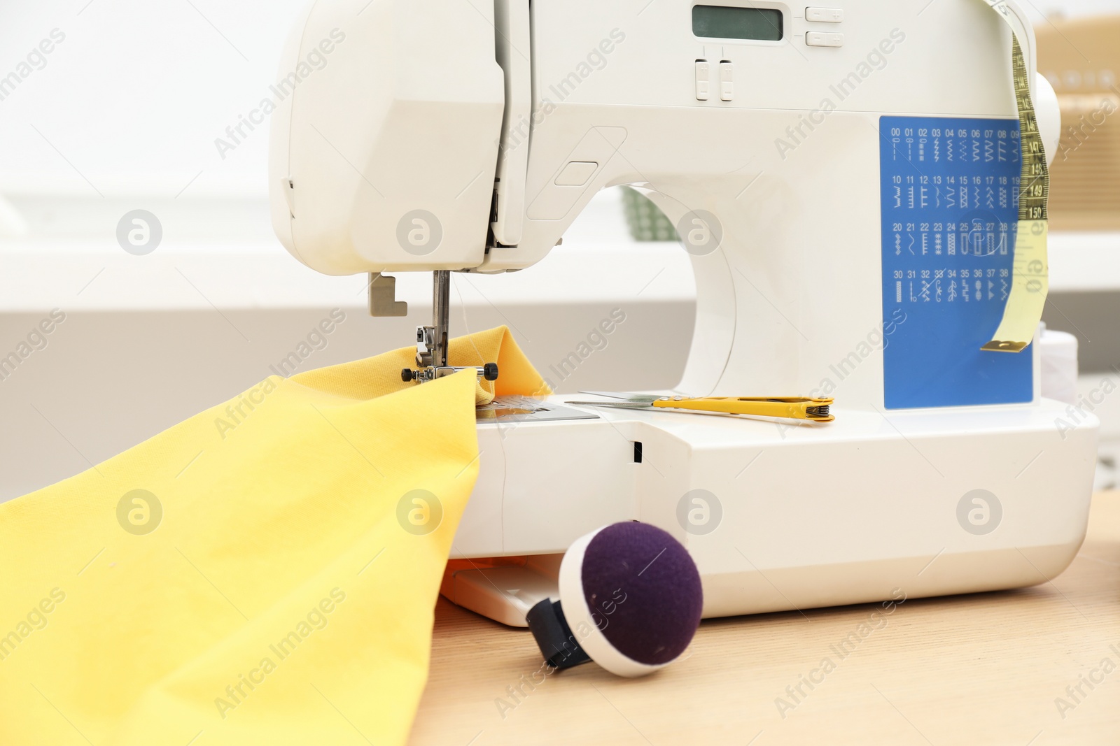 Photo of Sewing machine, tools and fabric on wooden table indoors, closeup