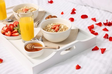 Photo of Tray with tasty breakfast and rose petals on bed at home