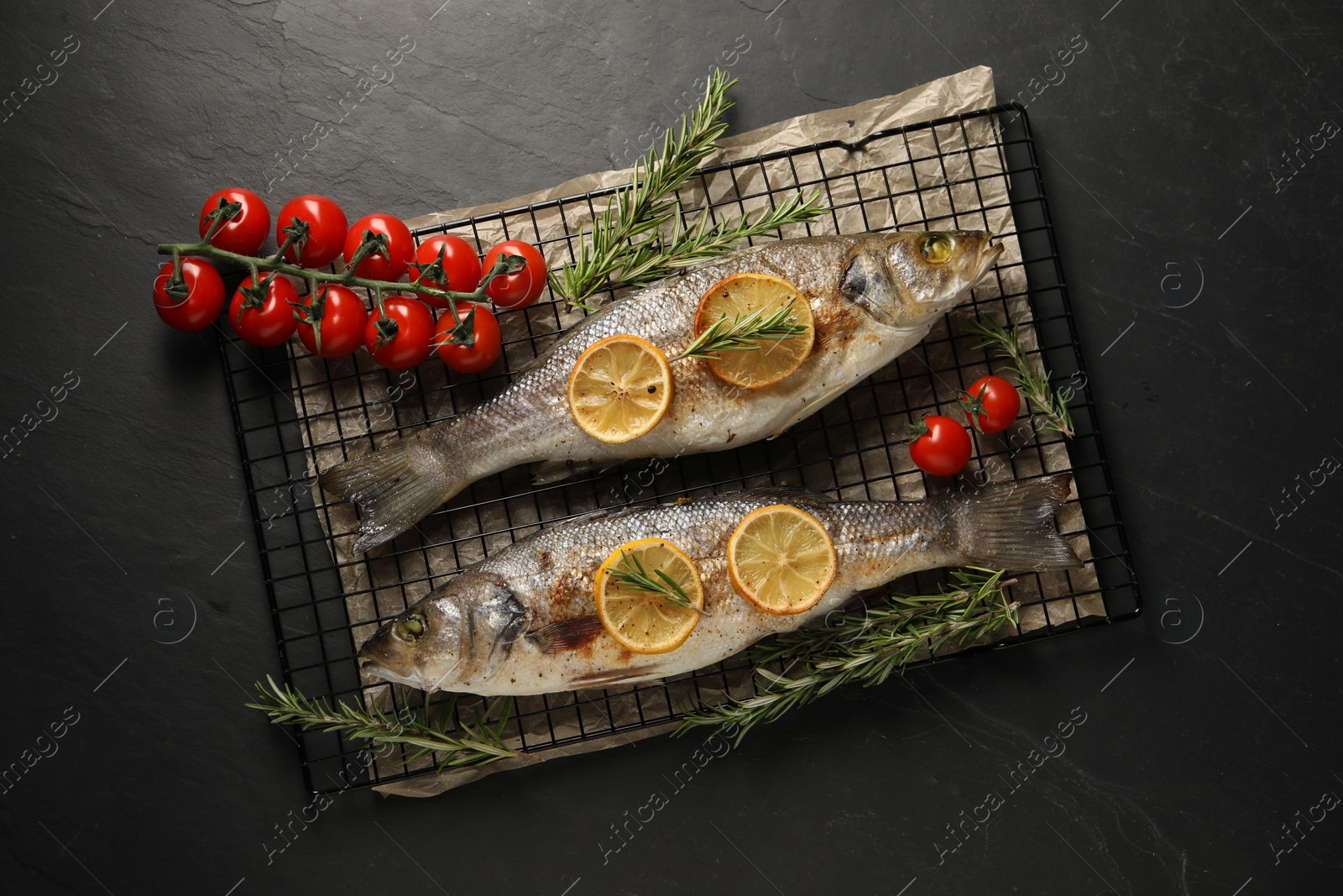 Photo of Baked fish with tomatoes, rosemary and lemon on black textured table, top view