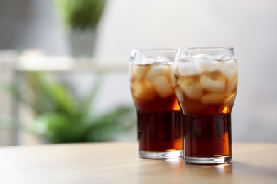 Glasses of cola with ice on table against blurred background, space for text