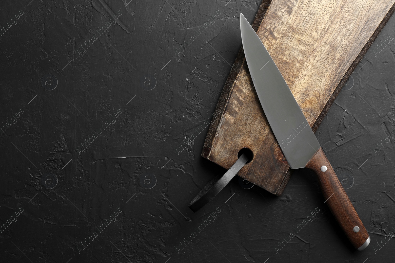 Photo of One sharp knife and board on dark textured table, top view. Space for text