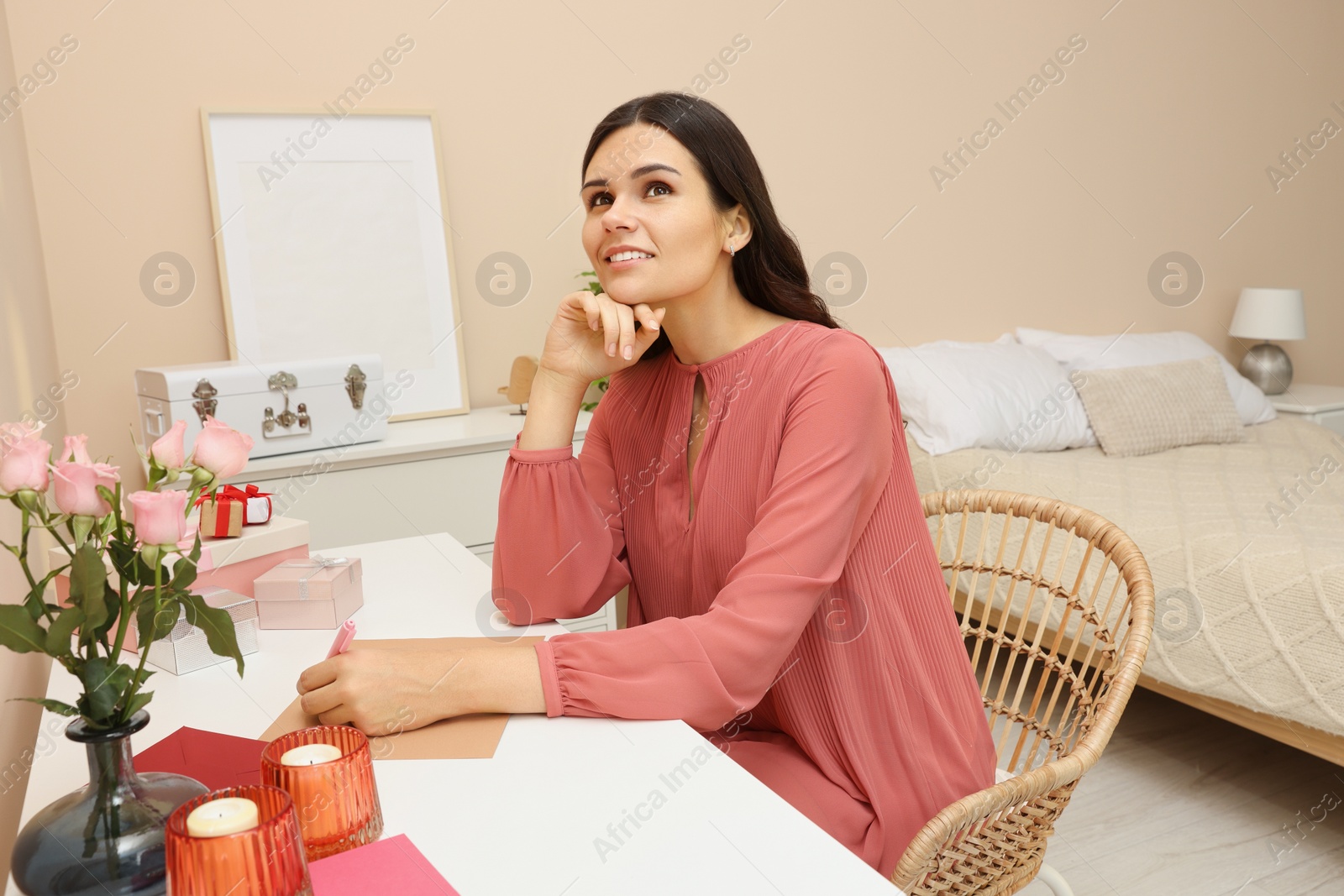 Photo of Young woman writing message in greeting card at table indoors