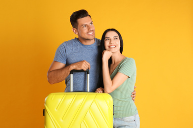 Happy couple with suitcase for summer trip on yellow background. Vacation travel