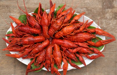 Plate with delicious red boiled crayfish on wooden table, top view