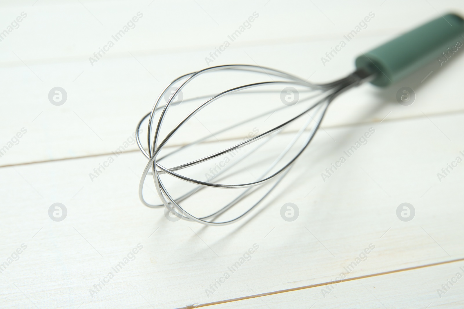 Photo of Metal whisk on white wooden table, closeup