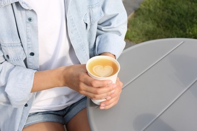 Photo of Coffee to go. Woman with paper cup of drink at grey table outdoors, closeup