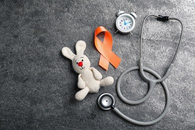 Photo of Orange ribbon, toy bunny, stethoscope and alarm clock on grey table, flat lay with space for text. Multiple sclerosis awareness