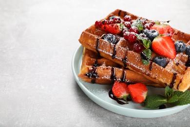 Delicious Belgian waffles with berries served on light grey table. Space for text