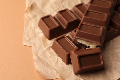 Photo of Parchment with delicious chocolate bars on light brown background, closeup