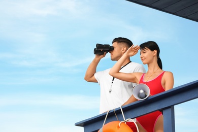 Photo of Lifeguards with megaphone and binocular on watch tower against blue sky
