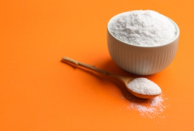 Photo of Bowl and spoon with salt on orange background, closeup. Space for text