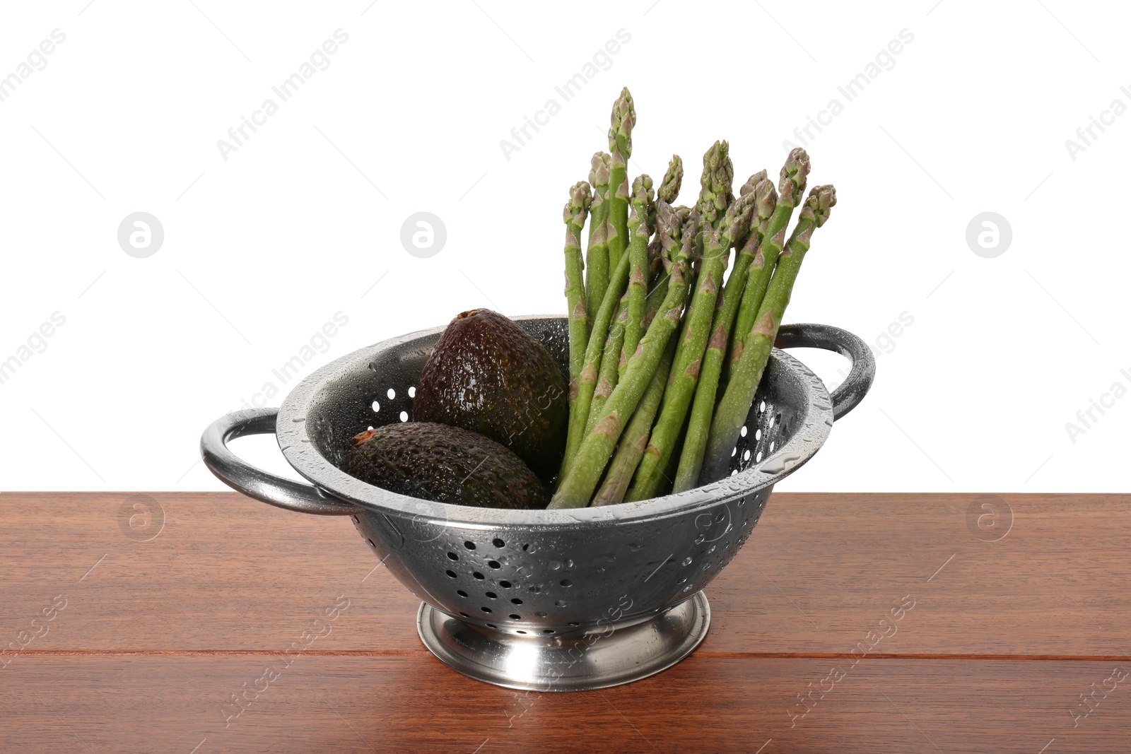 Photo of Metal colander with asparagus and avocados on wooden table against white background