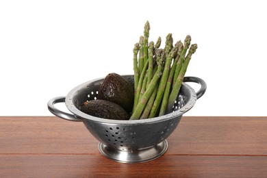 Photo of Metal colander with asparagus and avocados on wooden table against white background