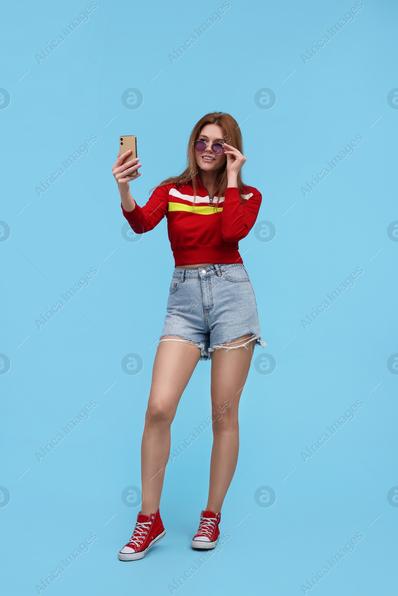 Photo of Beautiful woman in sunglasses taking selfie on light blue background