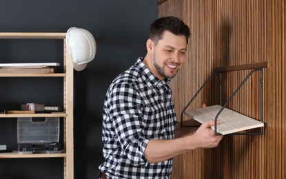 Photo of Handsome working man setting shelf indoors. Home repair