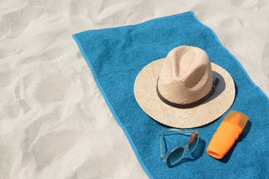 Photo of Soft blue towel, sunglasses, straw hat and bottle of sunblock on sandy beach