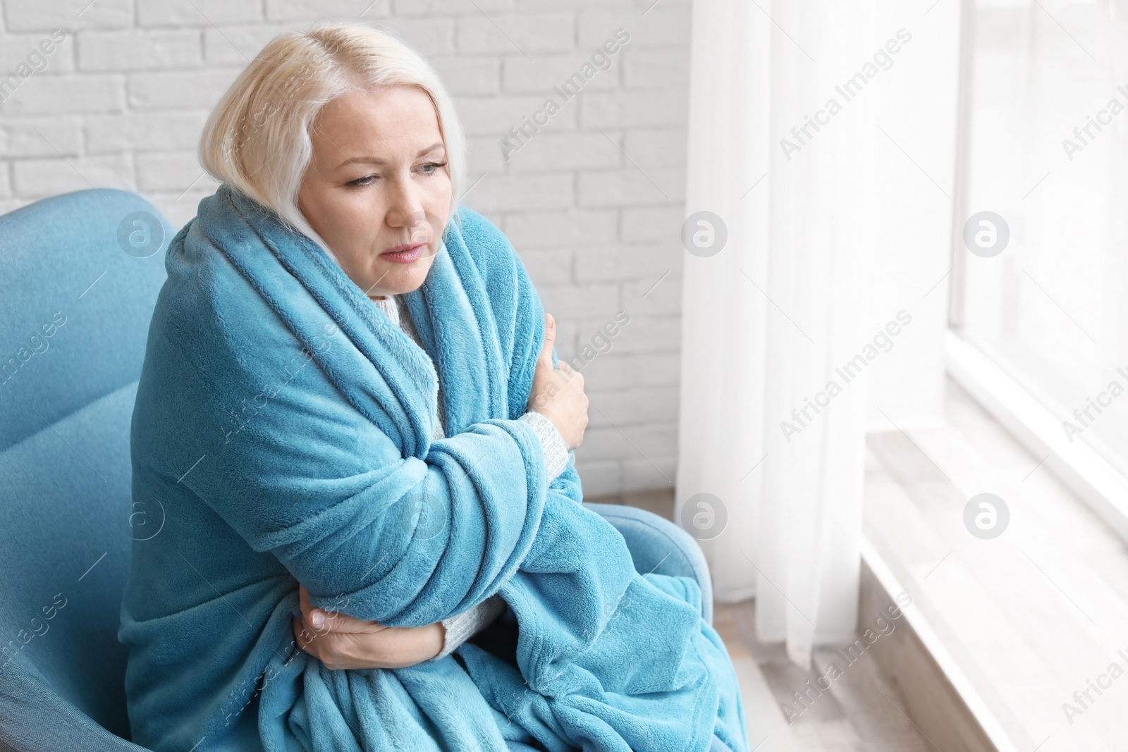 Photo of Mature woman wrapped in blanket suffering from cold at home