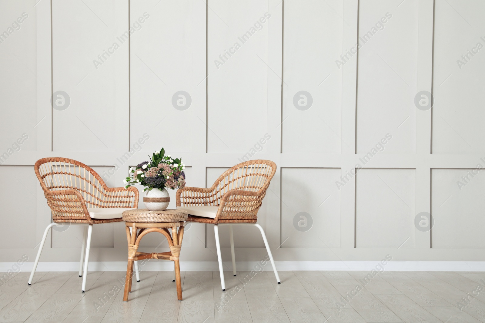 Photo of Simple room interior with set of wicker furniture, beautiful flowers and empty wall. Space for design