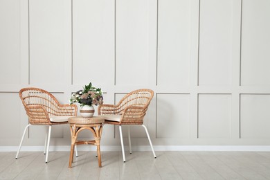 Photo of Simple room interior with set of wicker furniture, beautiful flowers and empty wall. Space for design