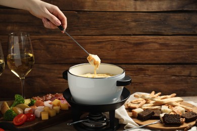 Woman dipping piece of bread into fondue pot with melted cheese at table with snacks, closeup