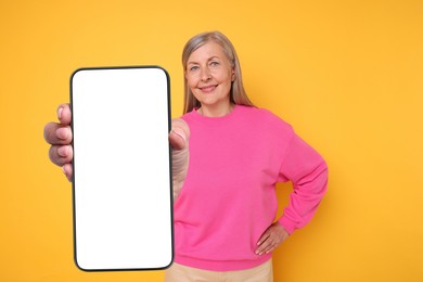 Happy mature woman showing mobile phone with blank screen on golden background. Mockup for design