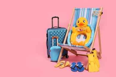 Photo of Deck chair, suitcases and beach accessories on pink background, space for text