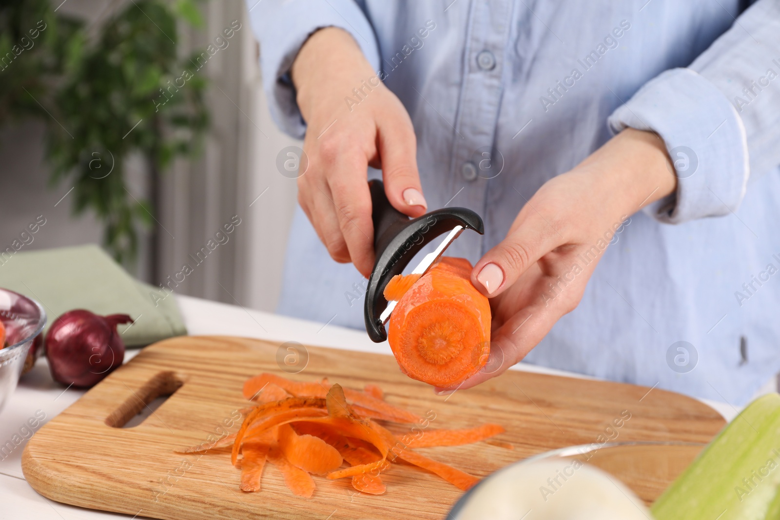 Photo of Woman peeling fresh carrot at table indoors, closeup