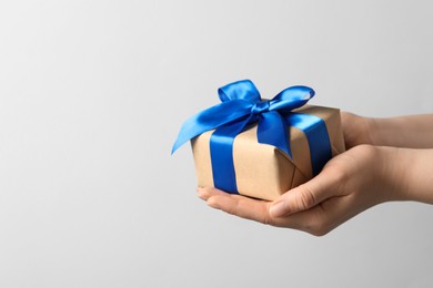 Photo of Woman holding gift box with blue bow on light grey background, closeup. Space for text