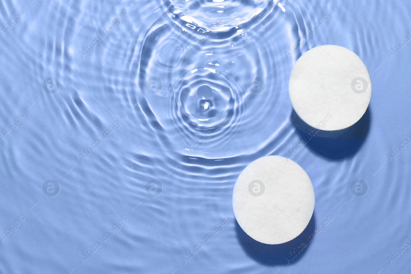 Image of Cotton pads in micellar water on light blue background, top view