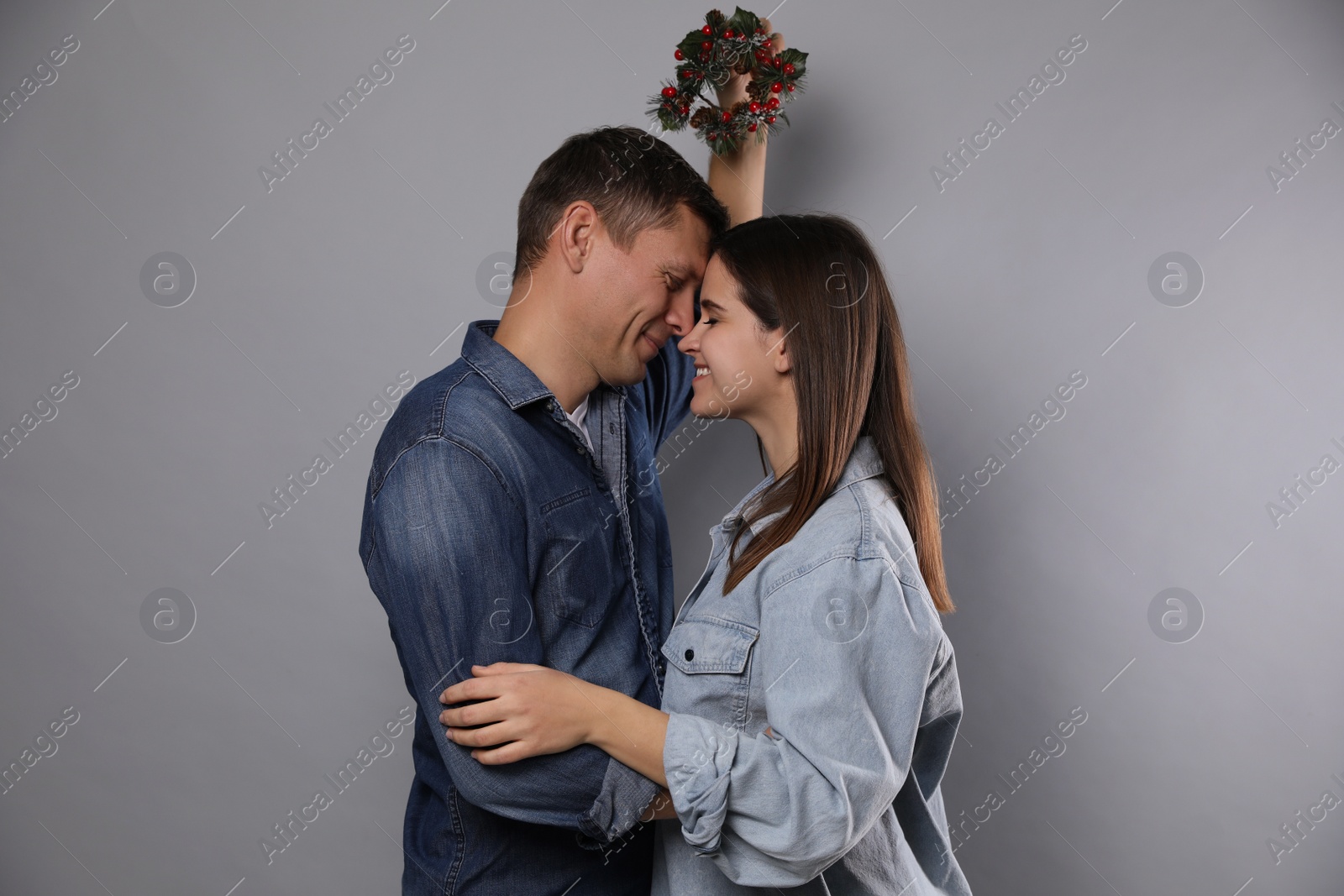 Photo of Happy couple standing under mistletoe wreath on grey background