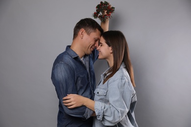 Happy couple standing under mistletoe wreath on grey background