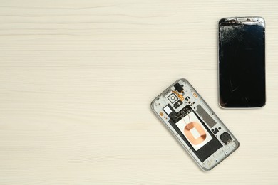Photo of Damaged smartphone on white wooden background, flat lay with space for text. Device repairing