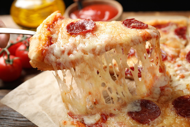Photo of Taking slice of tasty pepperoni pizza on wooden table, closeup