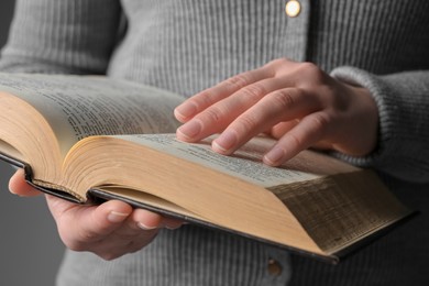 Woman reading Bible against grey background, closeup