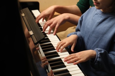 Young woman with child playing piano, closeup. Music lesson