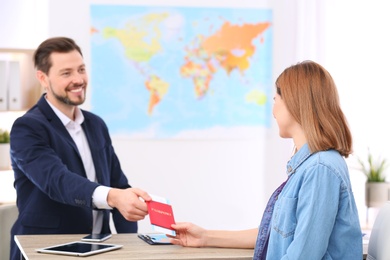 Photo of Male manager giving passport with ticket to client in travel agency