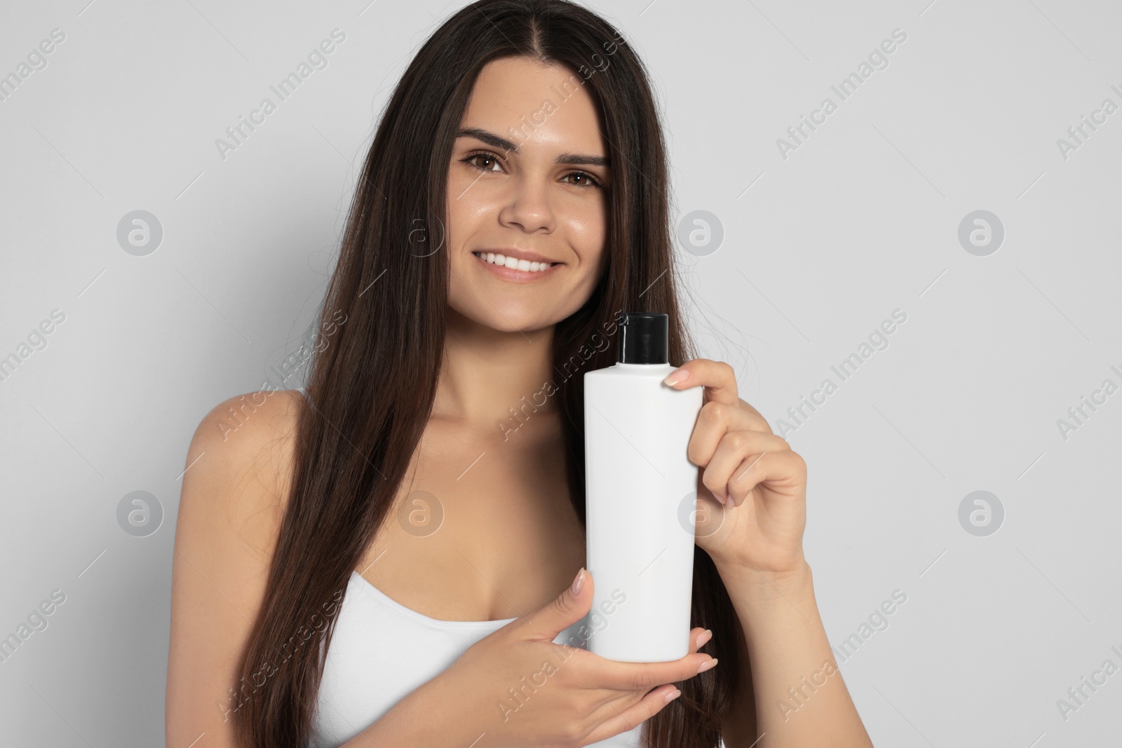 Photo of Beautiful young woman holding bottle of shampoo on white background